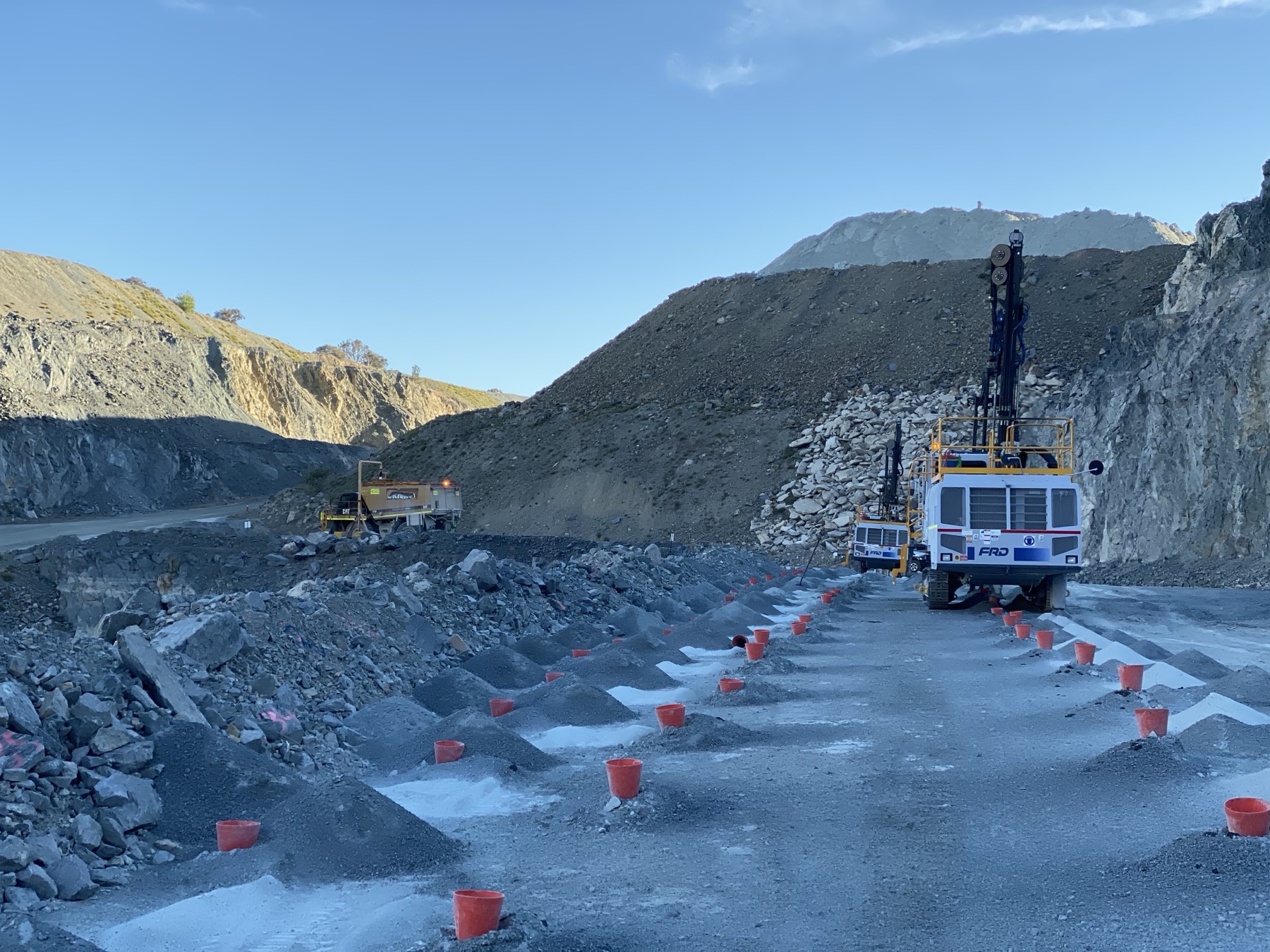 Stemmed and coned blast pattern running toward a drill rig at golden hour