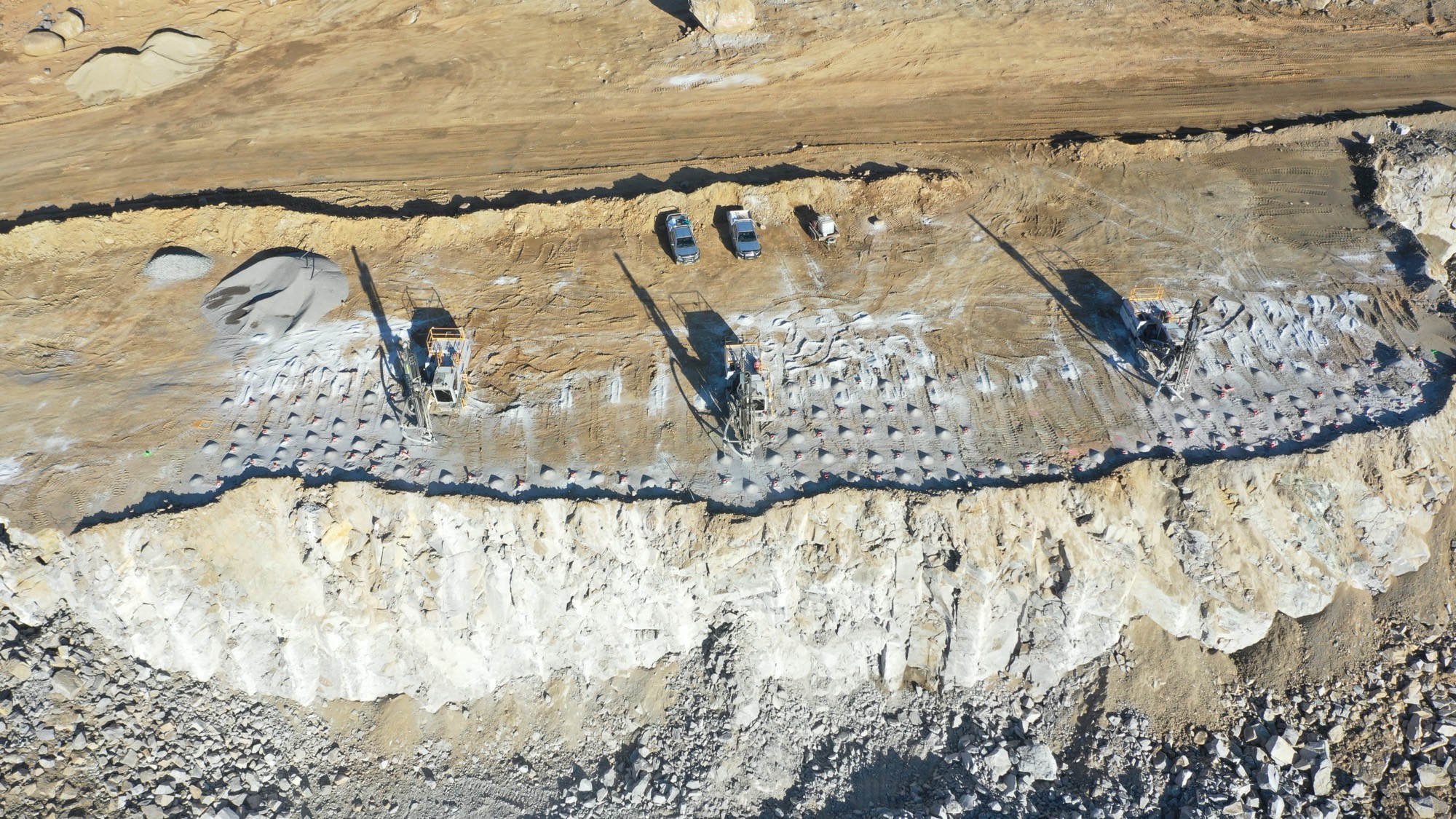 Aerial view straight down onto a drilled and stemmed blast pattern with rigs and light vehicles