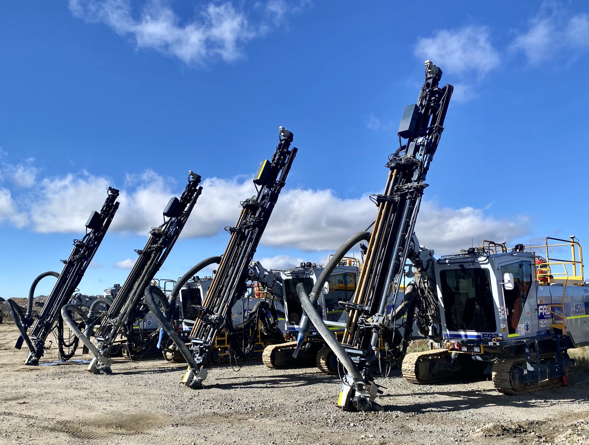 A line of Southern Explosives drill rigs with masts raised against a blue sky