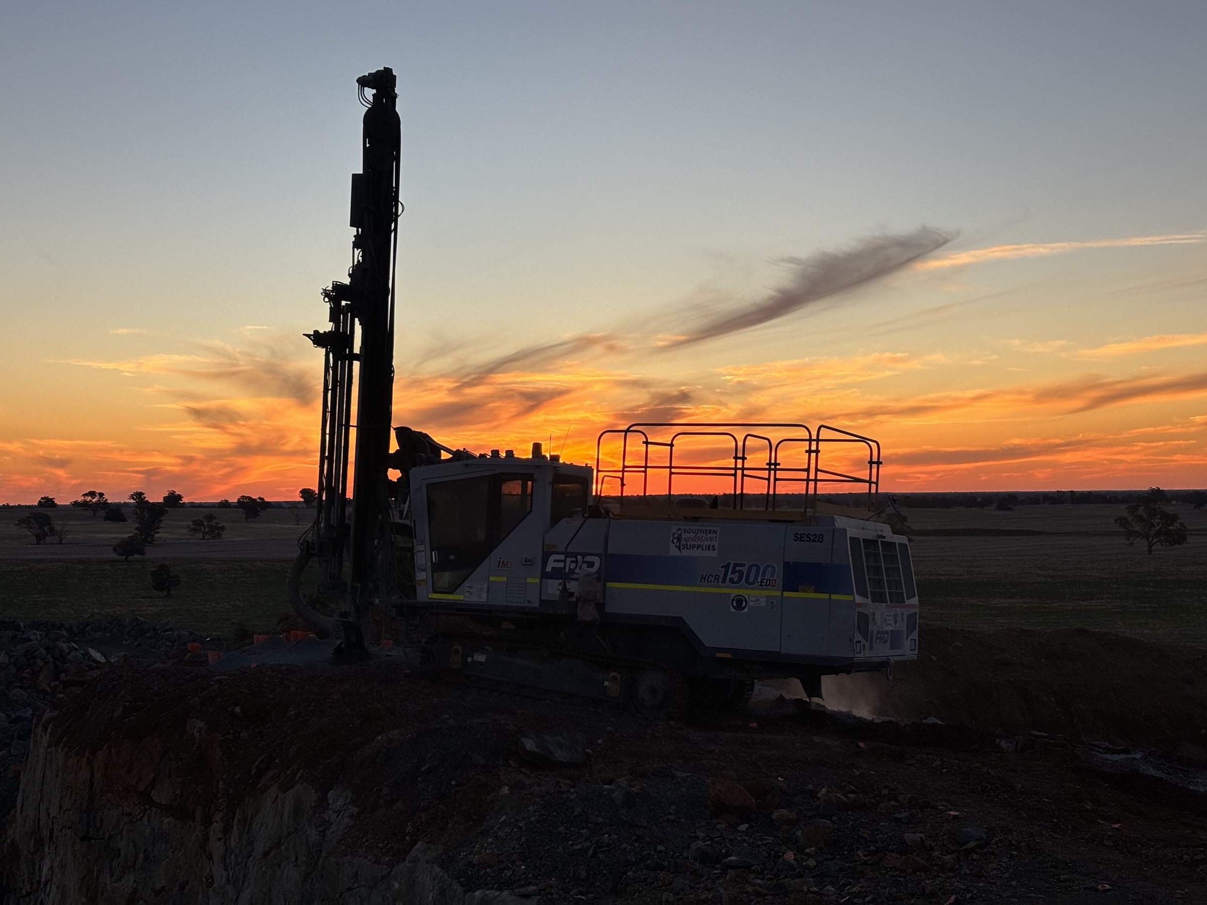 Southern Explosives drill rig silhouetted against an orange sunset